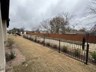 Landscaped backyard with a black metal fence, grass, and trees.