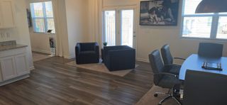 A modern living space with dark wood flooring, navy blue armchairs, and a small meeting table in a bright setting.