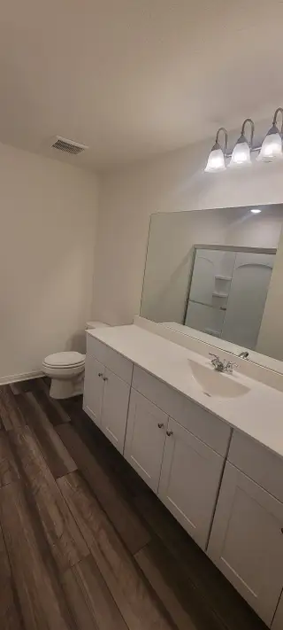 A sleek bathroom with elegant lighting, white vanity, and wood-style flooring.
