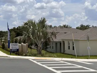 A modern, beige home with a palm tree in Cascades by D.R. Horton, Davenport, FL, showcasing new community living.