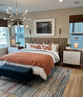 A modern bedroom with a tufted headboard, stylish chandelier, warm accents, and sleek furnishings.