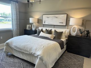A cozy bedroom featuring a plush bed with layered pillows, modern lamps, and abstract art, creating a serene retreat.