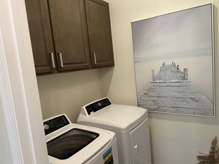 A cozy laundry room featuring a modern washer and dryer, wooden cabinets, and serene wall art of a pier.