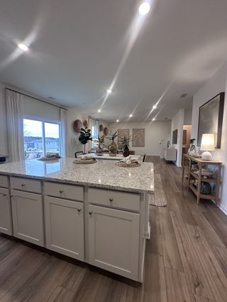 Model Home A spacious kitchen with a granite island, white cabinetry, and wood flooring, elegantly lit with recessed lighting.