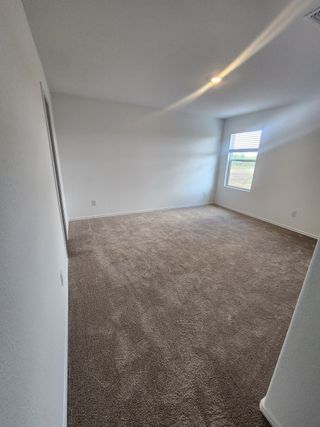 A spacious carpeted room with neutral walls, recessed lighting, and a large window offering natural light.