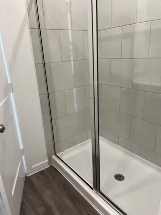 Model Home A sleek shower with glossy tiles and a chrome-framed glass door, set against modern wood flooring.