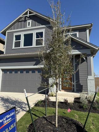 A charming gray home with a gable roof and manicured lawn in Double Creek Crossing – Craftsman Series by David Weekley Homes (Round Rock, TX).