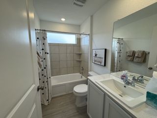A cozy bathroom featuring light cabinetry, a tiled bathtub, polka dot shower curtain, and modern fixtures.