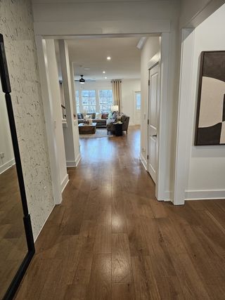 Model Home A welcoming hallway with rich wood flooring leading to a spacious, light-filled living area with an open-concept layout.