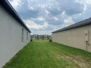 Street view A spacious lawn between modern homes in Balm Grove: The Executives by Lennar, with a backdrop of a cloudy sky (Wimauma, FL).