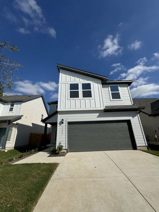 A striking modern farmhouse-style home with a bold black garage door and clean white siding in Longview by Taylor Morrison (Del Valle, TX).