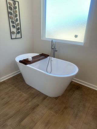 A serene bathroom featuring a freestanding tub, wooden floor, and stylish leaf artwork.