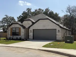 A newly built, light-stone home in Davis Ranch by Pulte Homes (San Antonio, TX), featuring a dark gray garage door, stone and brick accents, and fresh landscaping.
