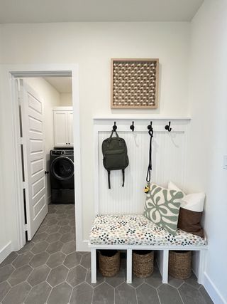 A cozy mudroom with a patterned bench, woven baskets, and spacious hooks, leading to a sleek laundry room.