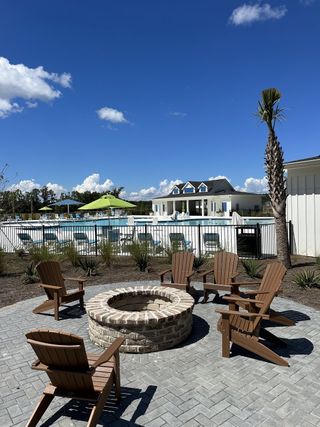 A relaxing outdoor fire pit area with Adirondack chairs and a pool view in Carolina Groves Townhomes by D.R. Horton (Moncks Corner, SC).