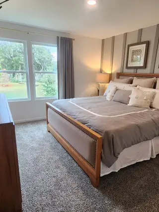A cozy bedroom with plush carpeting, a wooden bedframe, and soft lighting from a bedside lamp.