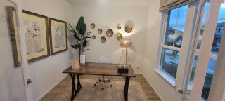 A cozy home office featuring wall art, leafy decor, a wooden desk, and ample natural light for an inviting workspace.
