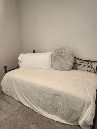 Model Home A cozy bedroom with a soft daybed, white linens, a plush accent pillow, and neutral walls.
