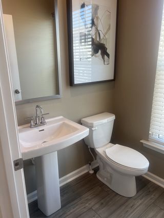 A contemporary bathroom featuring a pedestal sink, toilet, abstract artwork, and warm wood plank flooring.