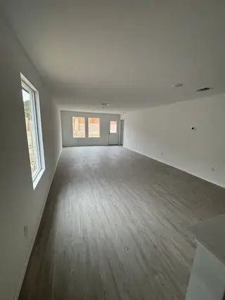 A spacious, open-plan room with light wood flooring, large windows, and neutral walls for a bright, welcoming feel.