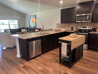Model Home A modern kitchen with dark wood cabinets, granite countertops, and stainless steel appliances flows into a bright living area.