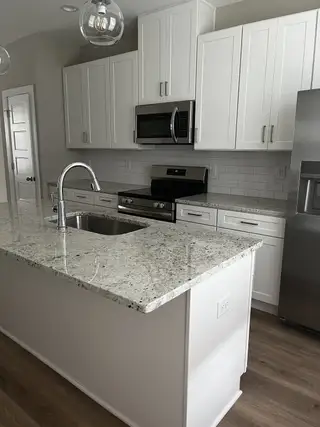 A modern kitchen featuring granite countertops, sleek white cabinetry, and stainless steel appliances.