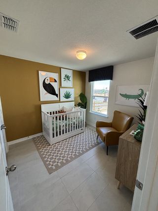 A cozy nursery featuring a white crib, tan accent wall, and playful decor with leafy artwork and a tufted armchair.