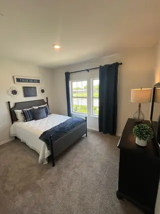 Model Home Cozy bedroom with a dark bedframe, plush carpet, and ample natural light. Decor adds a personal touch.