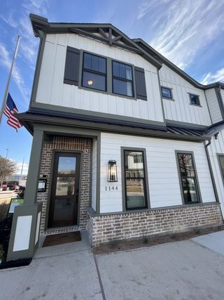 A modern white home with dark shutters in Collin Creek by Ashton Woods, featuring a brick facade in Plano, TX.