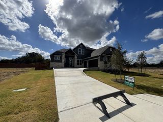 A beautiful modern home with a stone facade and expansive driveway in Broken Oak by Chesmar Homes (Georgetown, TX).