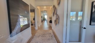 Model Home A bright hallway with wooden floors, unique wall decor, and modern lighting leading to a cozy living area with a Christmas tree.