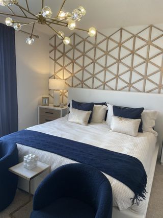 A modern bedroom with a geometric accent wall, plush bedding, and navy decor, accented by a chic chandelier.