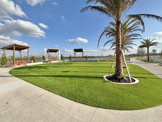Community Amenities A lush green park with palm trees and shaded seating areas in EverBe: Venture Townhomes by Lennar (Orlando, FL).
