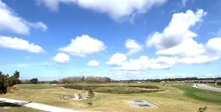A stunning view of the Indian River Preserve Golf Course with a bright blue sky dotted with fluffy white clouds. The lush green landscape and walking paths create a serene, inviting atmosphere