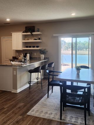 Model Home A cozy kitchen and dining area with wood flooring, granite counters, open shelving, and serene lake views.