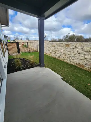 Model Home A cozy patio with concrete flooring overlooking a green lawn and stone wall, offering a relaxing outdoor space.