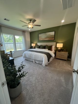 A cozy bedroom with a green accent wall, plush carpeting, and stylish decor, featuring a large window and ceiling fan.