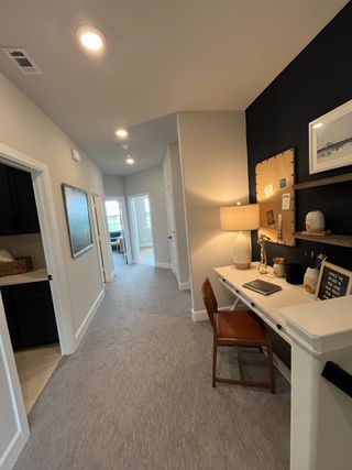 A cozy hallway with a built-in desk, accent wall, and warm lighting, leading to bright rooms.