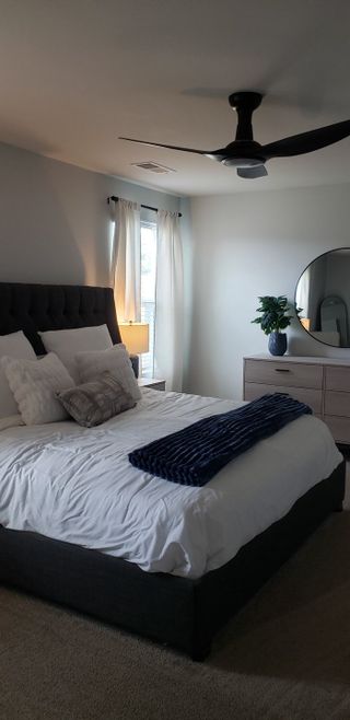 Model Home A modern bedroom with a plush bed, sleek fan, and elegant decor featuring a round mirror and soft lighting.