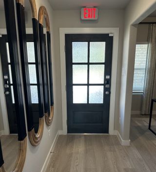 A modern entryway featuring a sleek black door with frosted glass panels and elegant mirrors reflecting light.