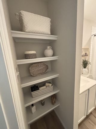 Model Home A neatly organized shelf nook with woven baskets and decorative pieces, adjacent to a bright bathroom vanity.