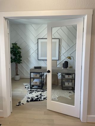 A chic home office with a geometric accent wall, glass door, and modern decor, featuring a cowhide rug and sleek desk.