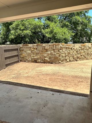 A serene backyard patio with a stone wall and lush greenery, providing a peaceful retreat in Clear Creek by Brohn Homes (Round Rock, TX).