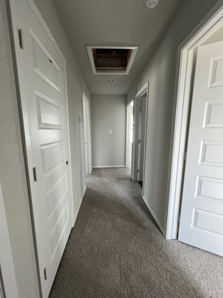Model Home A carpeted hallway with white doors and attic access, leading to multiple rooms.