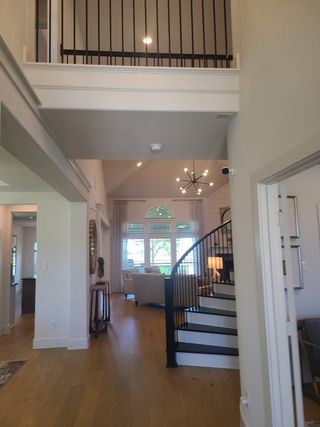 An elegant foyer with a curved staircase, modern light fixture, and open floor plan with large windows and airy ambiance.