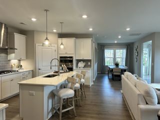 A modern kitchen with an island, sleek cabinetry, hardwood floors, and pendant lighting leading to a cozy dining area.