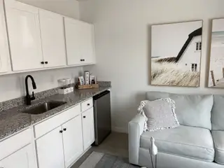 A cozy kitchenette with granite countertops, white cabinets, and cozy seating adorned with coastal artwork and modern fixtures.