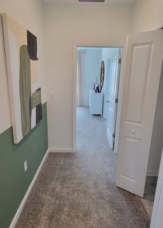 A tastefully decorated hallway with abstract art, leading to a bright room with plush carpeting and modern decor.