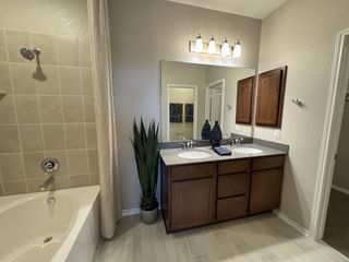 Model Home A modern bathroom with a spacious corner tub, dual sinks, wooden cabinets, and elegant fixtures.