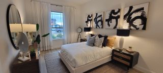A modern bedroom with abstract art, elegant lighting, and a cozy bed. Natural light floods through the window.